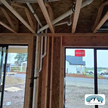 Interior view of a building under construction, featuring exposed wooden framing and white PVC plumbing pipes.