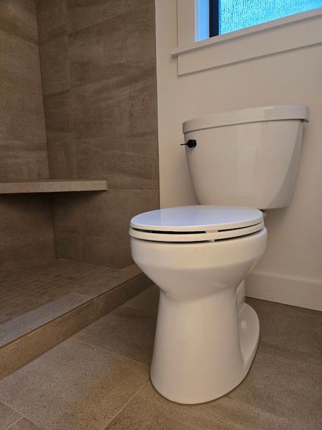 A white toilet positioned next to a tiled walk-in shower with a built-in bench in a bathroom.