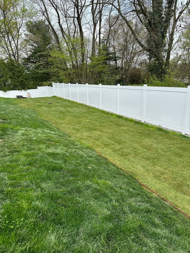 A white fence surrounds a lush green lawn in a backyard.