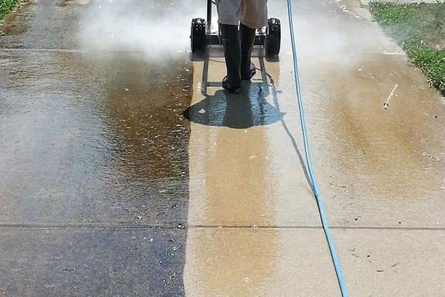 A person is cleaning a sidewalk with a machine.