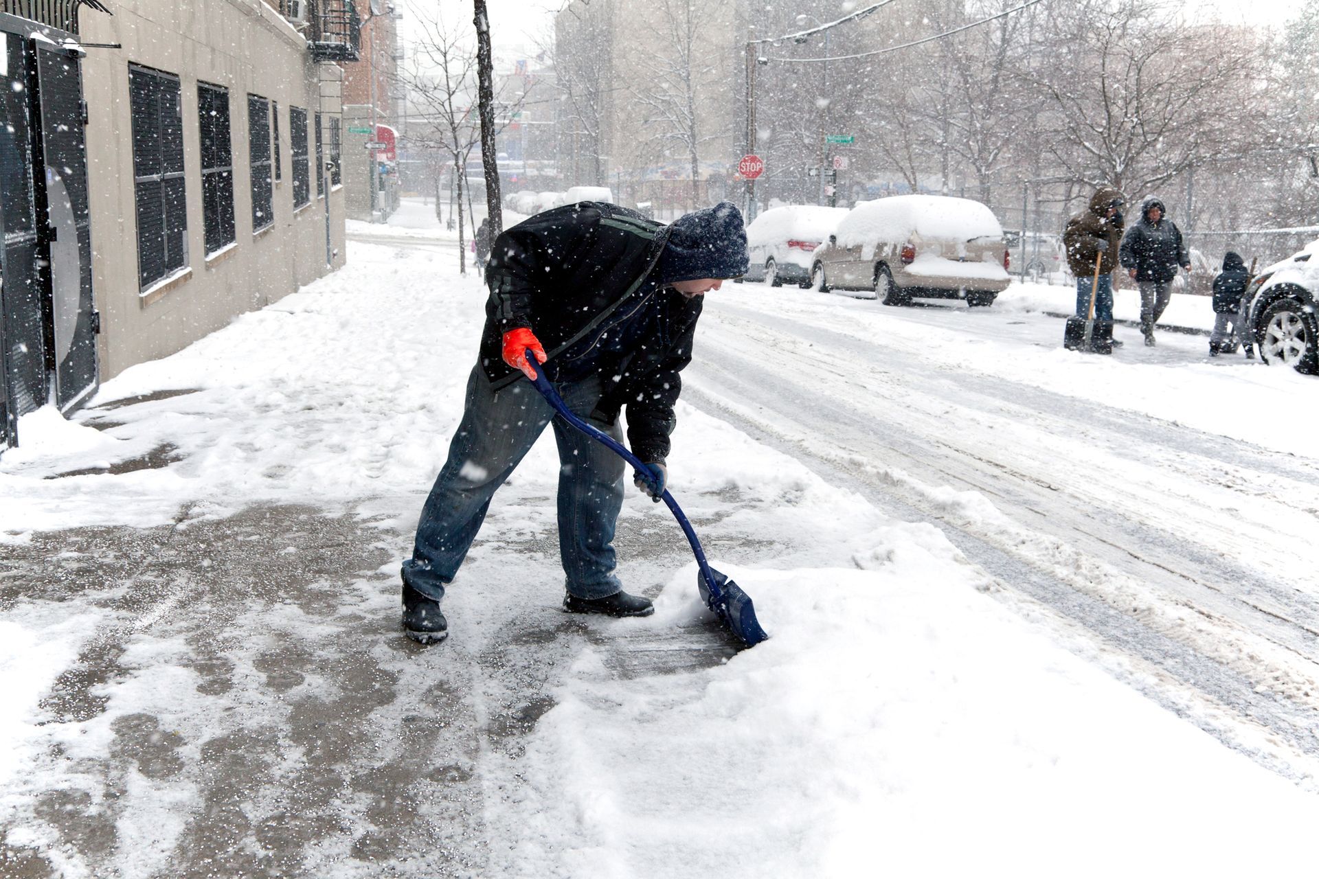 Person shoveling snow on a city sidewalk during a snowstorm
