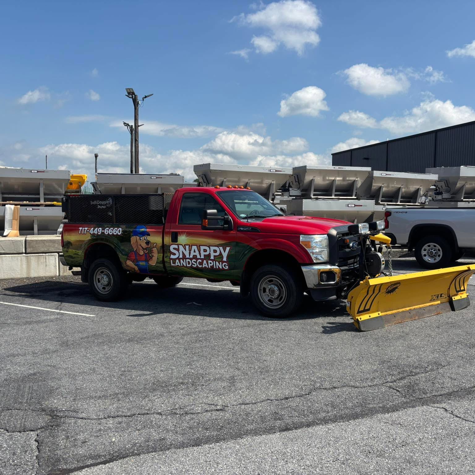 Red landscaping truck with snowplow, logo “Snappy Landscaping”, parked in lot under blue sky.