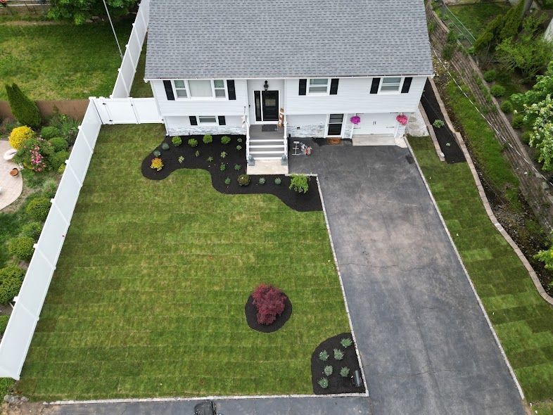 Aerial view of a white house with gray roof, green lawn, and a paved driveway.