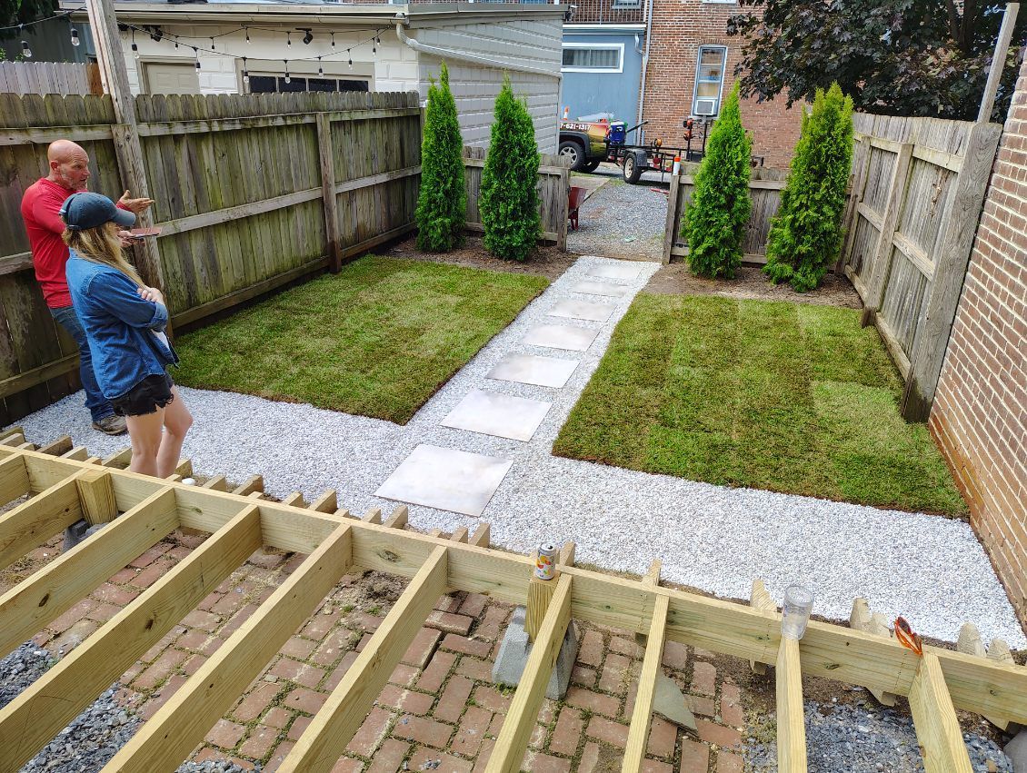 A man and a woman are standing in a backyard looking at a fence.