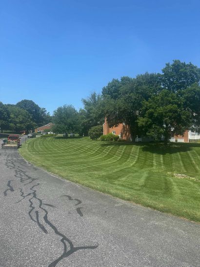 Lawn Care & Maintenance Curving gravel road beside manicured green lawn, large trees, and red-roofed houses under a blue sky