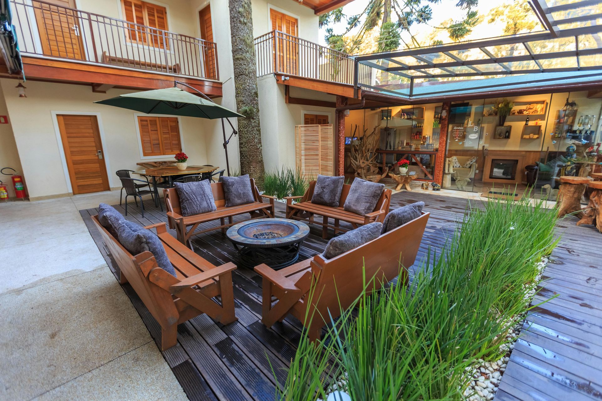 Outdoor courtyard with a fire pit, wooden bench seating, a patio table, and a covered terrace with greenery.