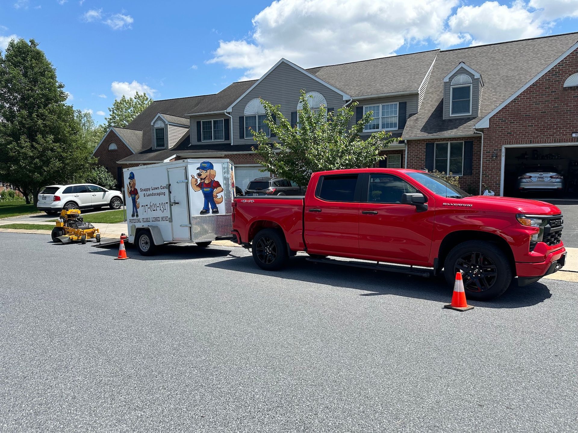 A red truck is parked in front of a house with a trailer attached to it.