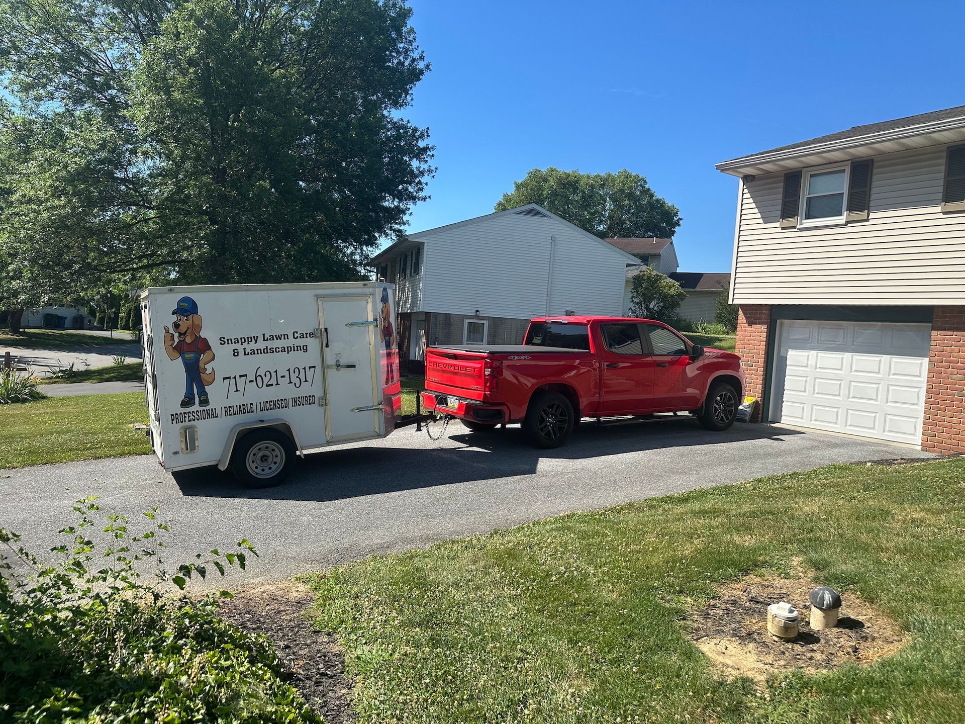 A red truck with a trailer attached to it is parked in front of a house.