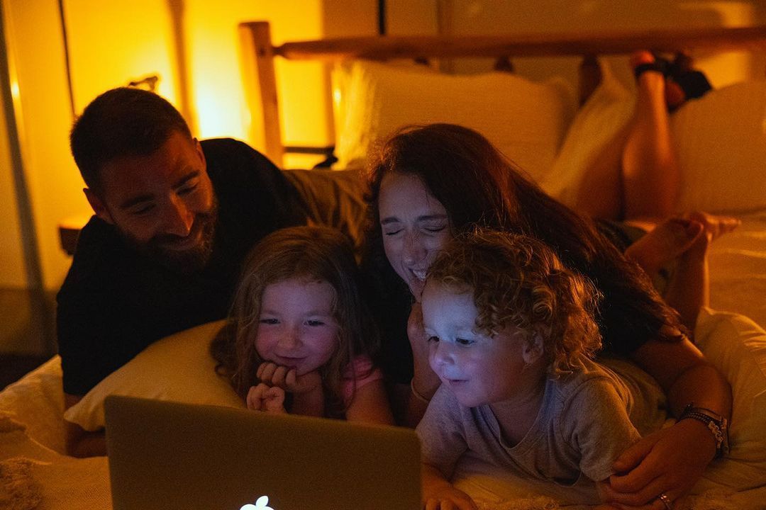 A family is laying on a bed looking at a laptop computer.