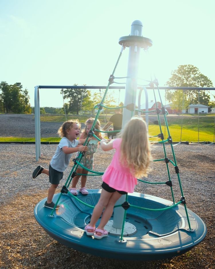 Three little girls are playing on a merry go round at a playground.