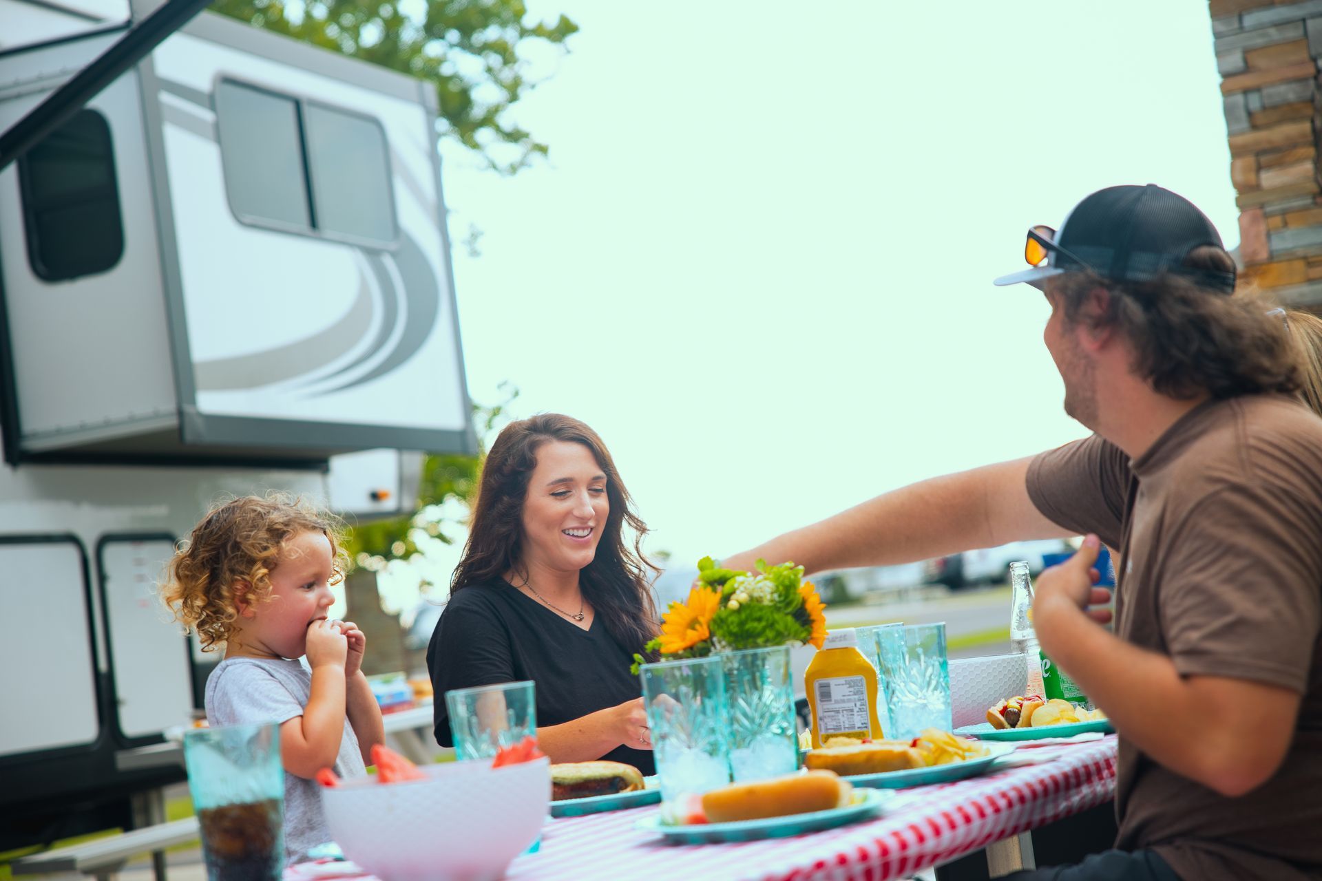 A family is sitting at a table with food in front of a rv.
