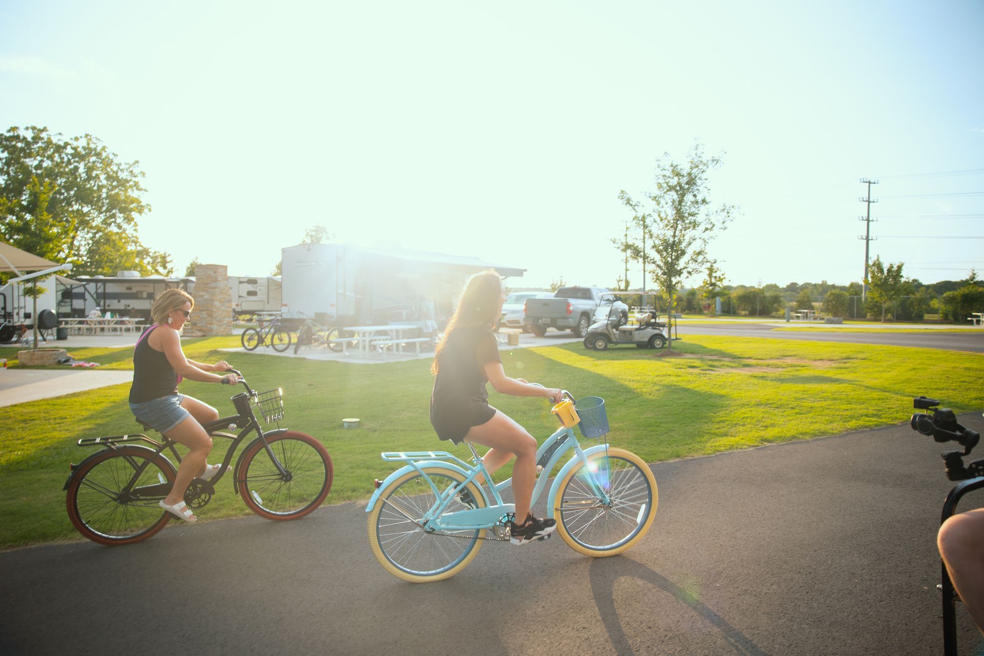 Two women are riding bicycles on a path in a park.