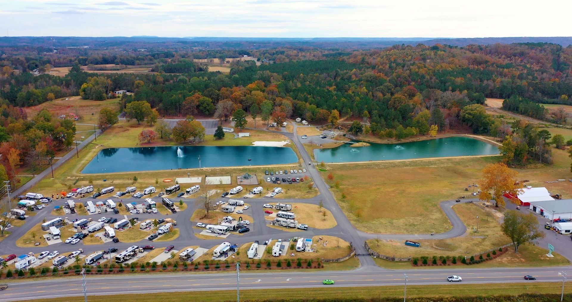 Aerial view of a recreational park with RVs parked near two ponds and autumn foliage.