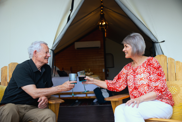 A man and a woman are toasting with wine glasses in front of a tent.