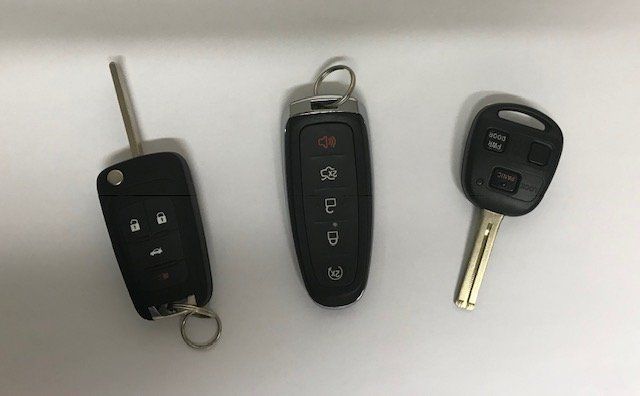 Three car keys are sitting on a white surface