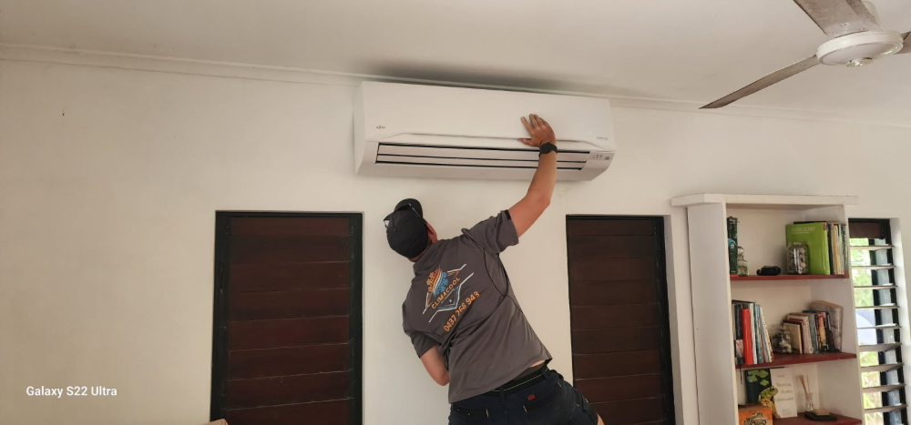 A person is working on an air conditioning unit mounted on a white wall— Climacool Air Conditioning in Trinity Beach, QLD