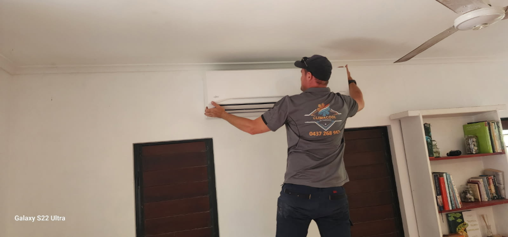 A man installs an air conditioning unit on a white wall inside a room— Climacool Air Conditioning in Trinity Beach, QLD
