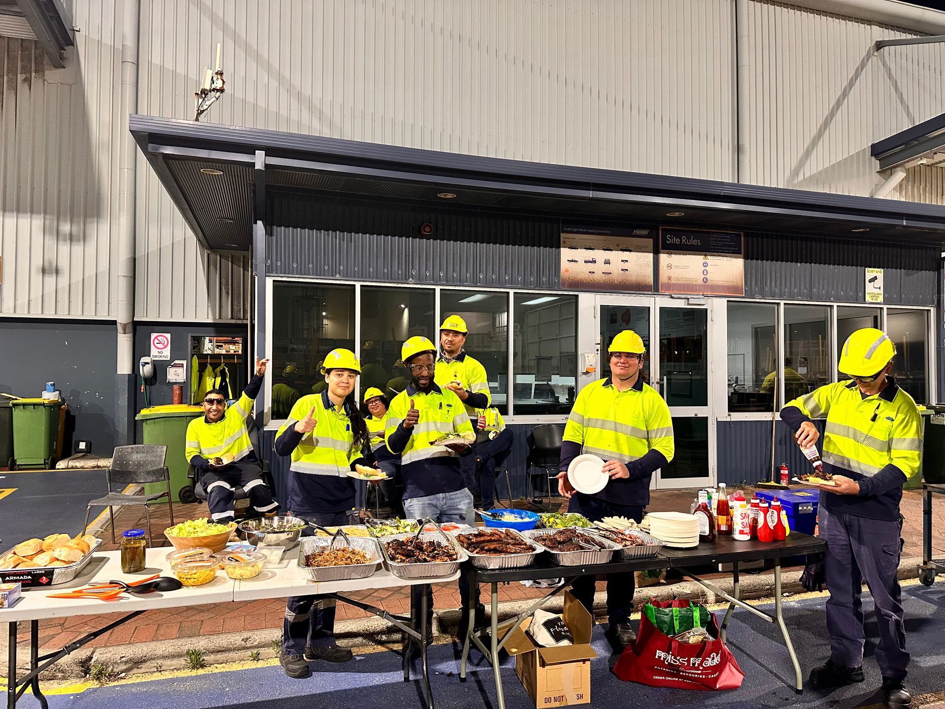 a group of happy construction workers standing around a table with bbq food