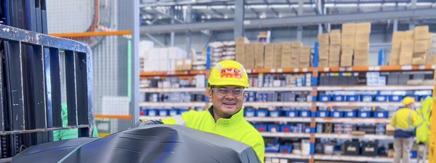 A man wearing yellow hi-vis and a hard hat loading a forklift in a warehouse