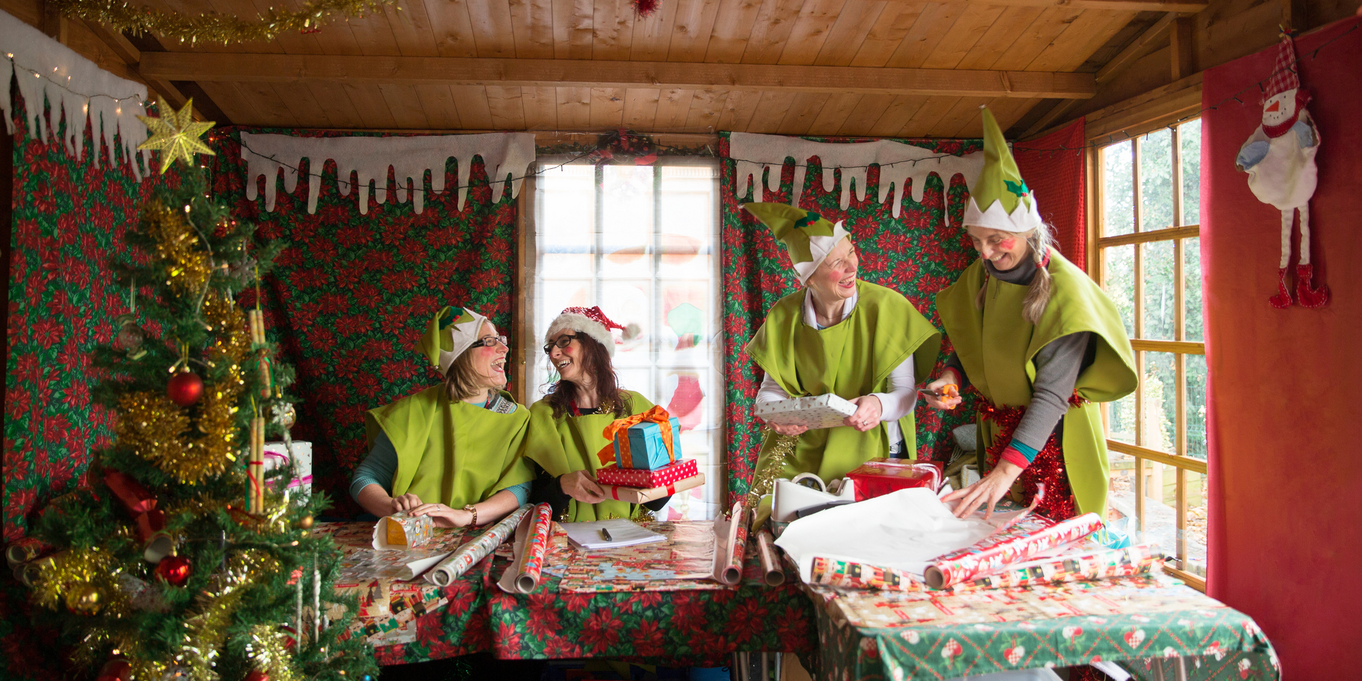4 of Santa's elves building toys in Santa's workshop. They are wearing green elf outfits. 
