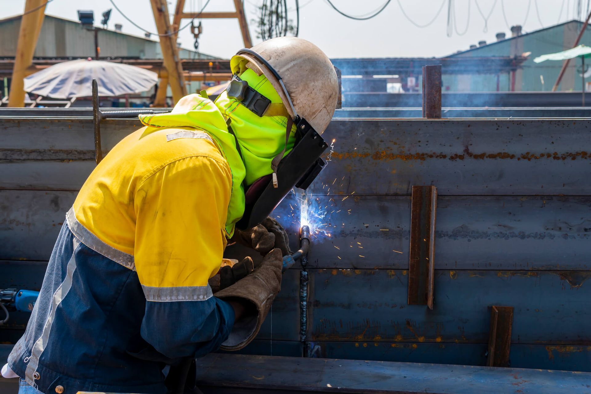 Manufacturing worker dressed in a red and black shirt with a yellow hi-vis on top and a yellow safety helmet to the side. He has it hand on his face and looks very stressed.