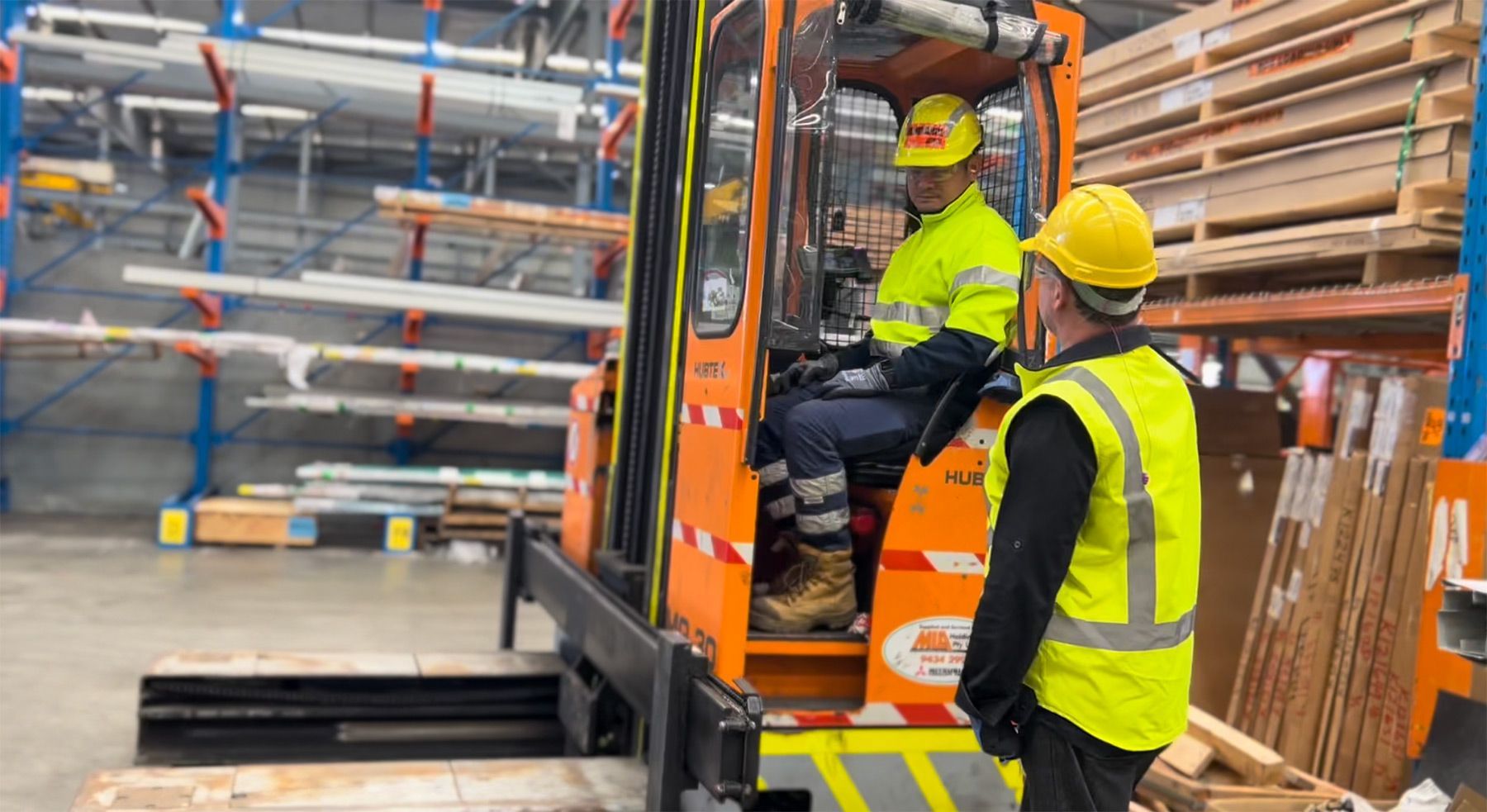 Forklift driver and coworker discussing forklift hazards while wearing PPE in a warehouse.