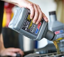 Hand pouring motor oil from a gray bottle.
