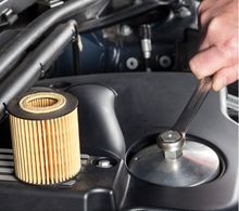 Hand with wrench loosening oil filter cap on a car engine. New filter nearby.