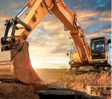 Yellow excavator digging into dirt at a construction site with cloudy sky background.