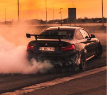 Black BMW drifting, tires smoking on asphalt at sunset.