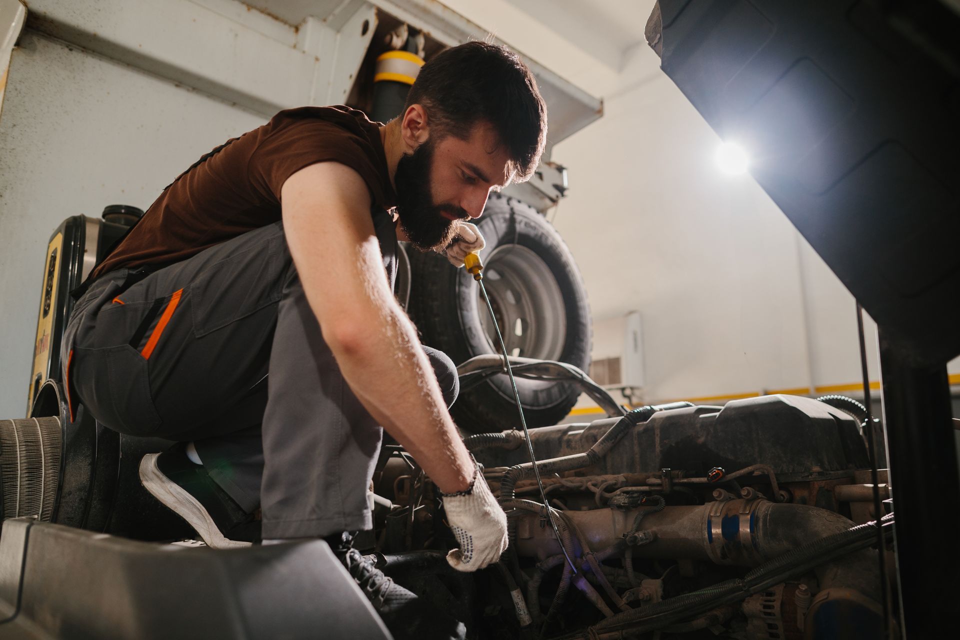 Mechanic working on a car engine in a garage; crouched down, using a tool. Mechanic working on a car engine in a garage; crouched down, using a tool.