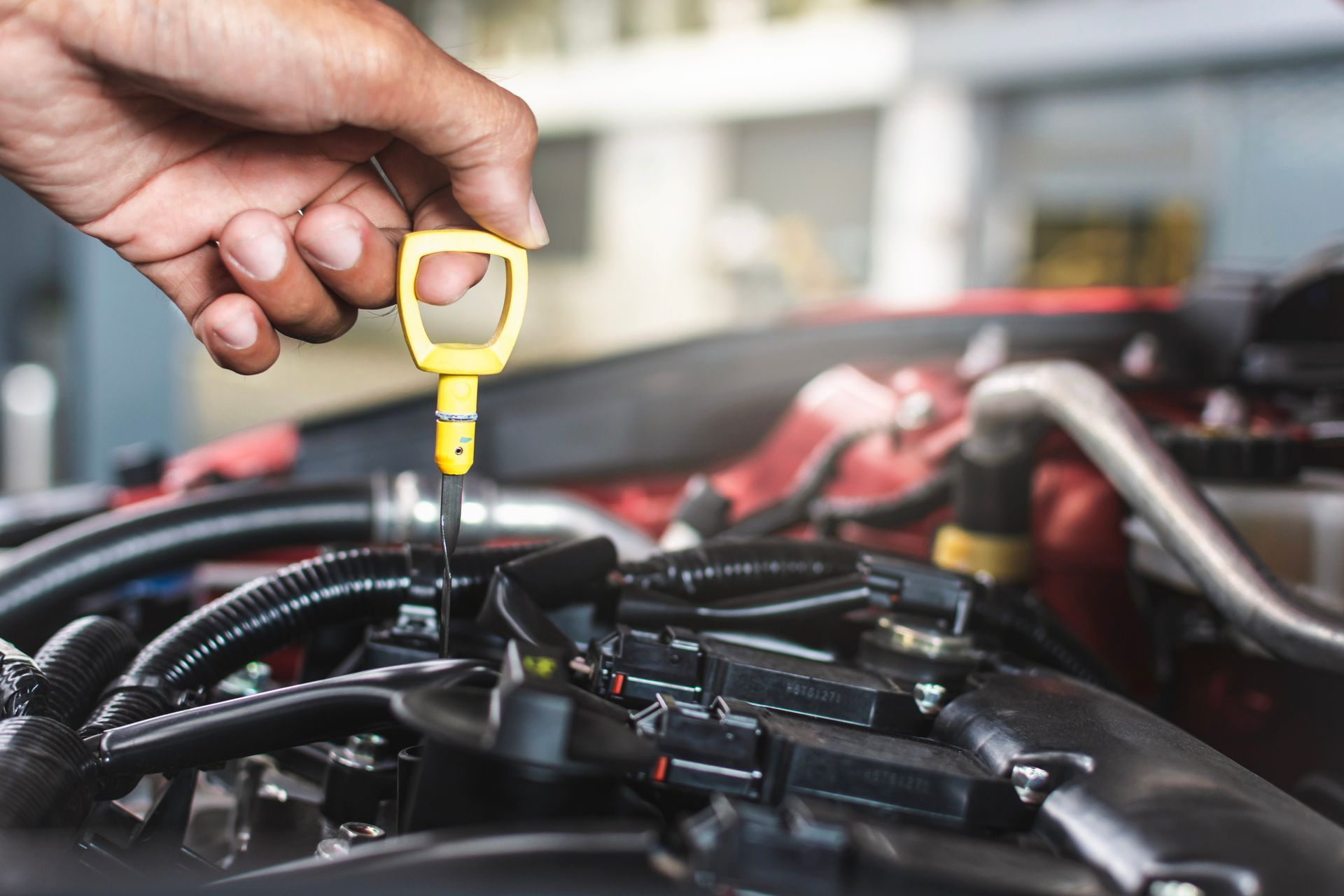 Hand checking engine oil with yellow dipstick in car engine bay.