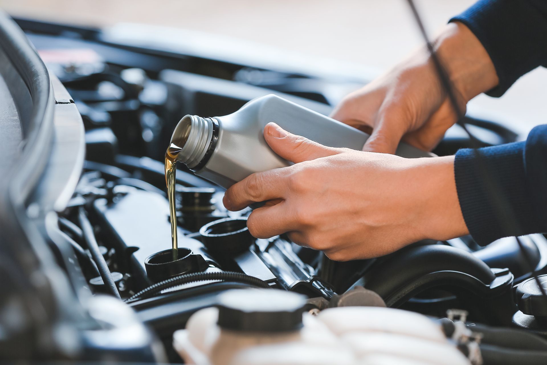 Hands pouring oil from a bottle into a car engine, in an open engine bay.