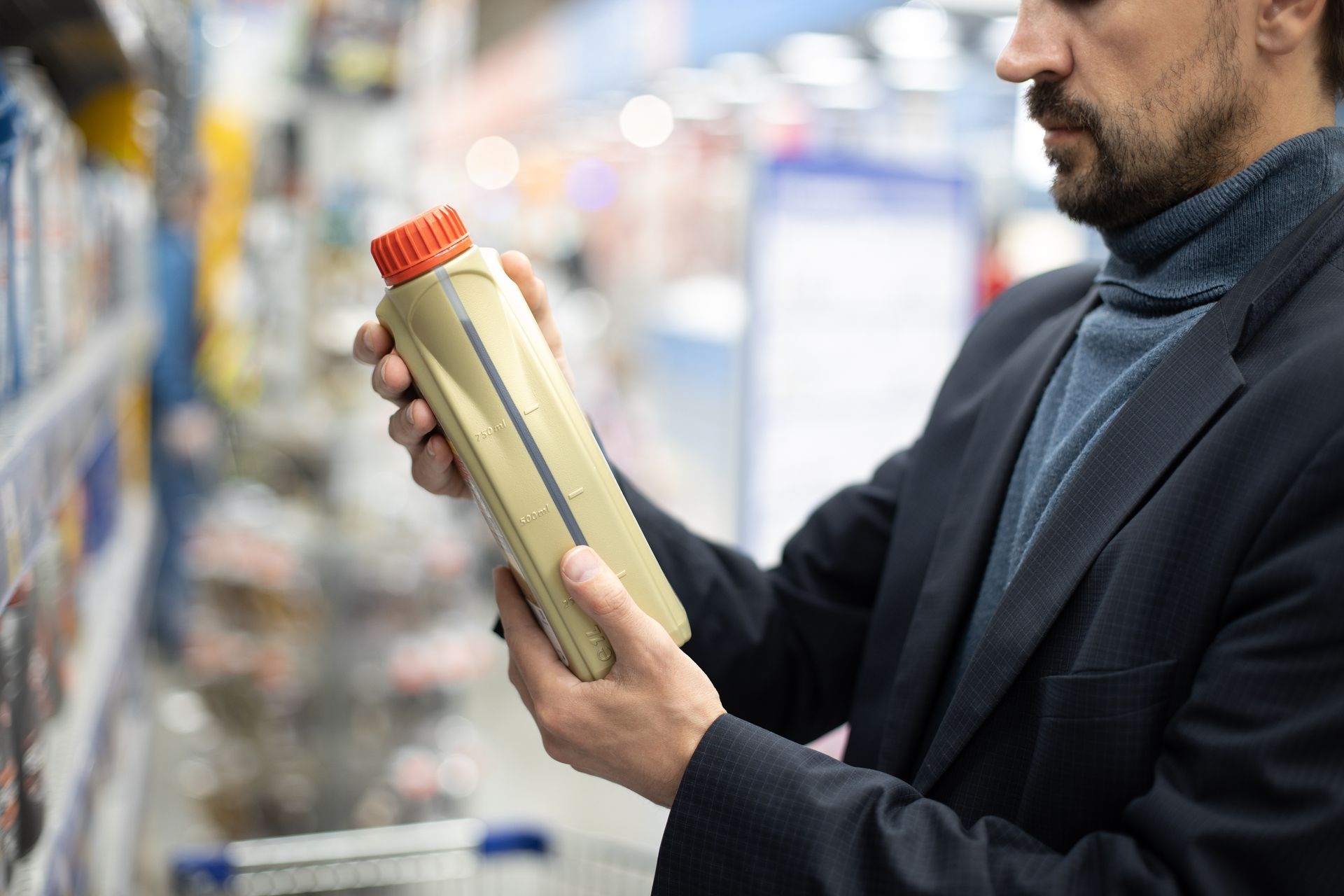 Man in a blazer examines motor oil bottle in a store aisle, selecting a product. Man in a blazer examines motor oil bottle in a store aisle, selecting a product.