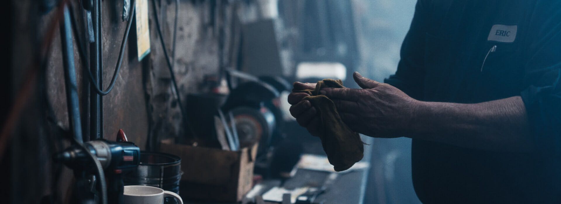 Person in workshop wipes hands with a rag. Workshop tools in the background.