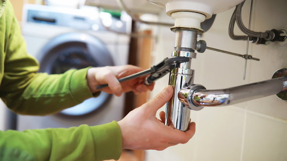 A person is fixing a sink with a wrench.