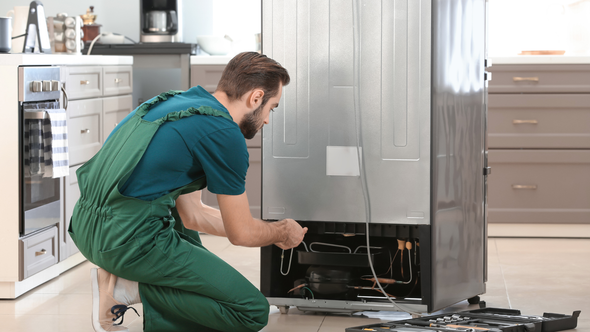 A man is repairing a refrigerator in a kitchen.