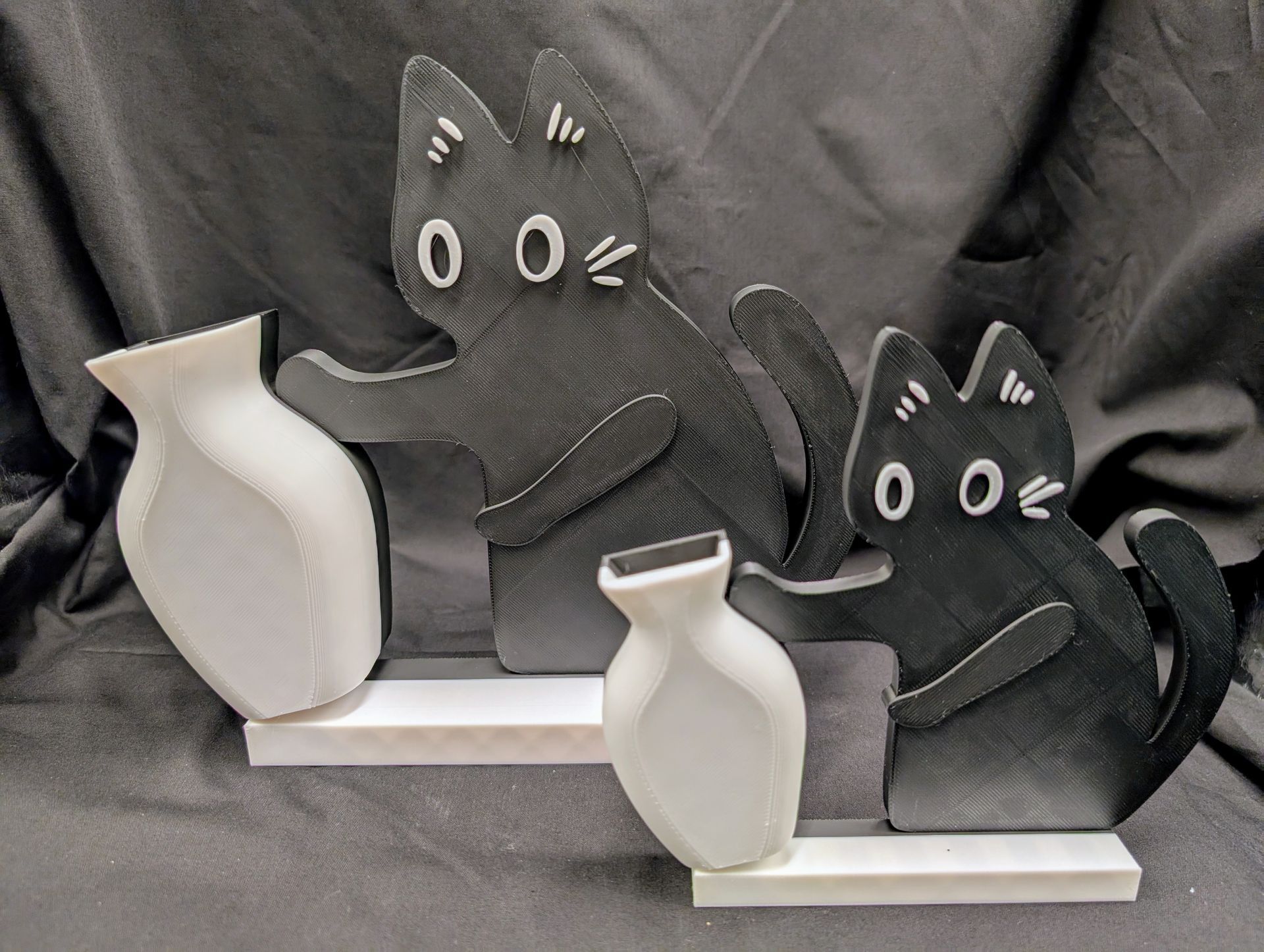 Big black cat model pushing over a small white vase.