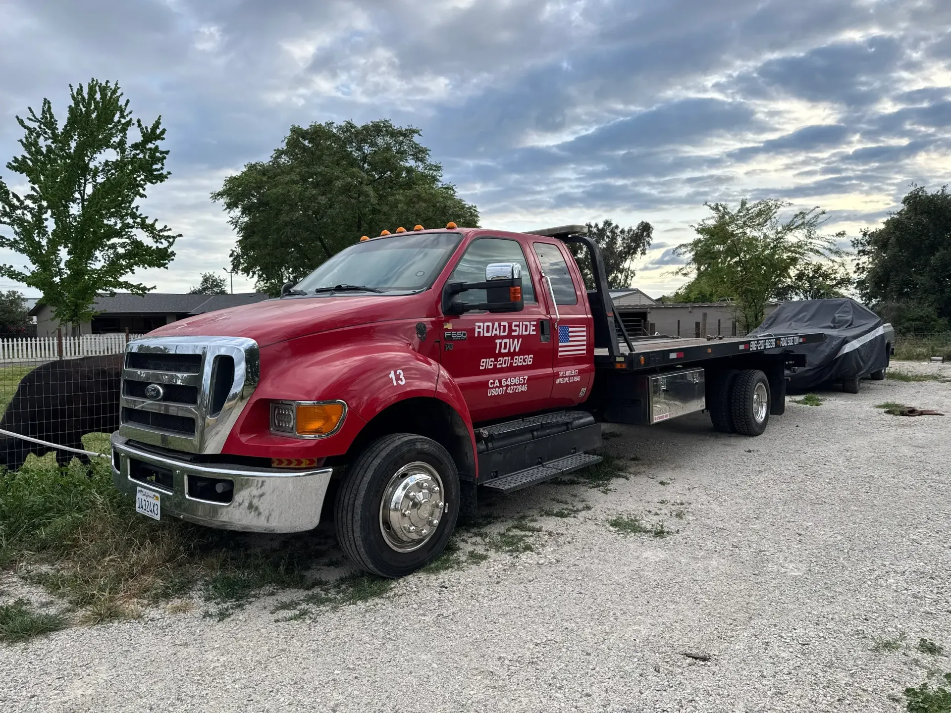 A red tow truck is parked in a gravel lot next to a car.