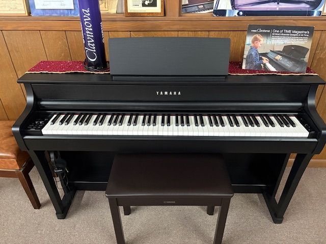 Black Yamaha digital piano with sheet music and bench, on display.