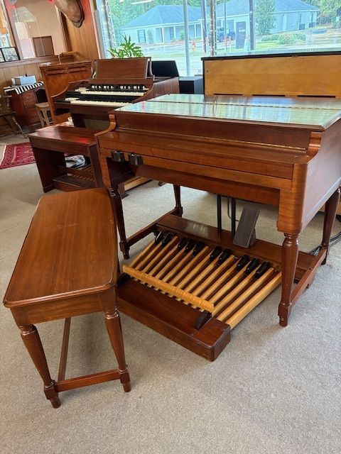 An antique organ with pedals, bench, and wooden cabinet, in a room with other instruments.