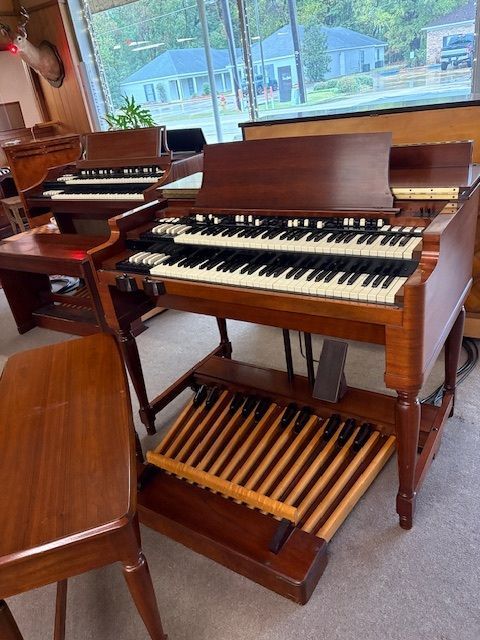 A vintage Hammond organ with two keyboards, foot pedals, and a wooden bench in a showroom.