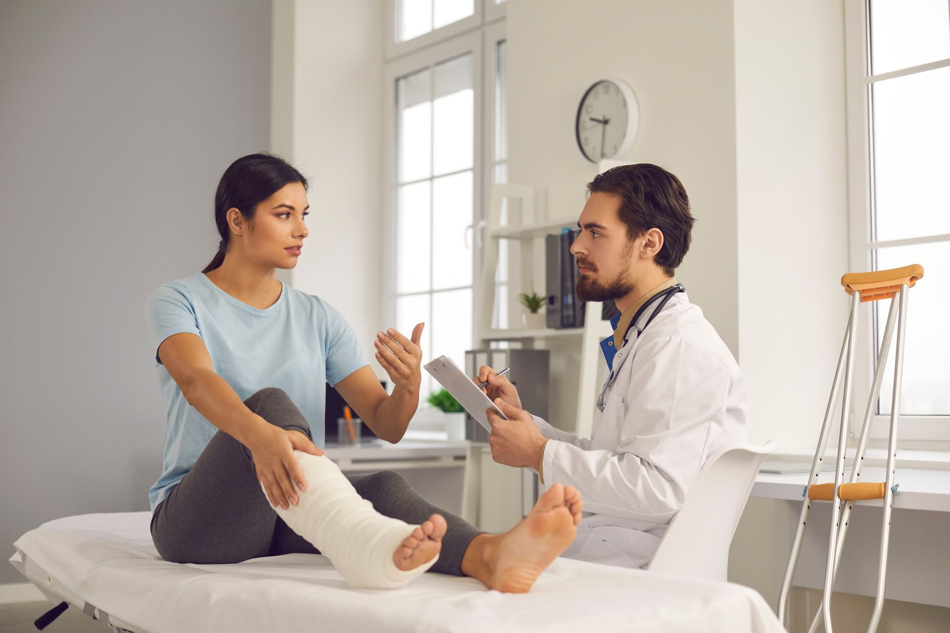 A woman with a broken leg is sitting on a bed talking to a doctor.