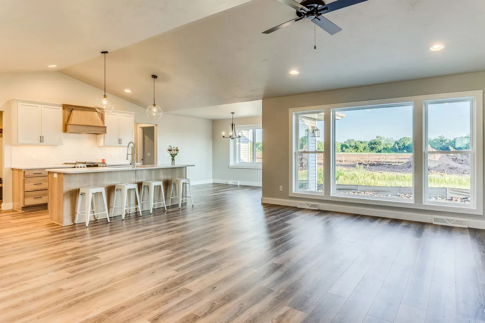 Spacious, open-concept kitchen and living area with wood floors, white cabinets, and large windows.