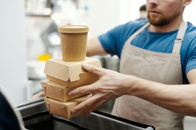 A man is holding a stack of boxes and a cup of coffee.