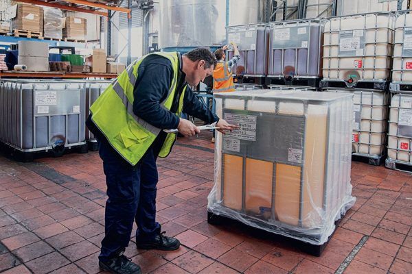 a man in a yellow vest is looking at a box in a warehouse .