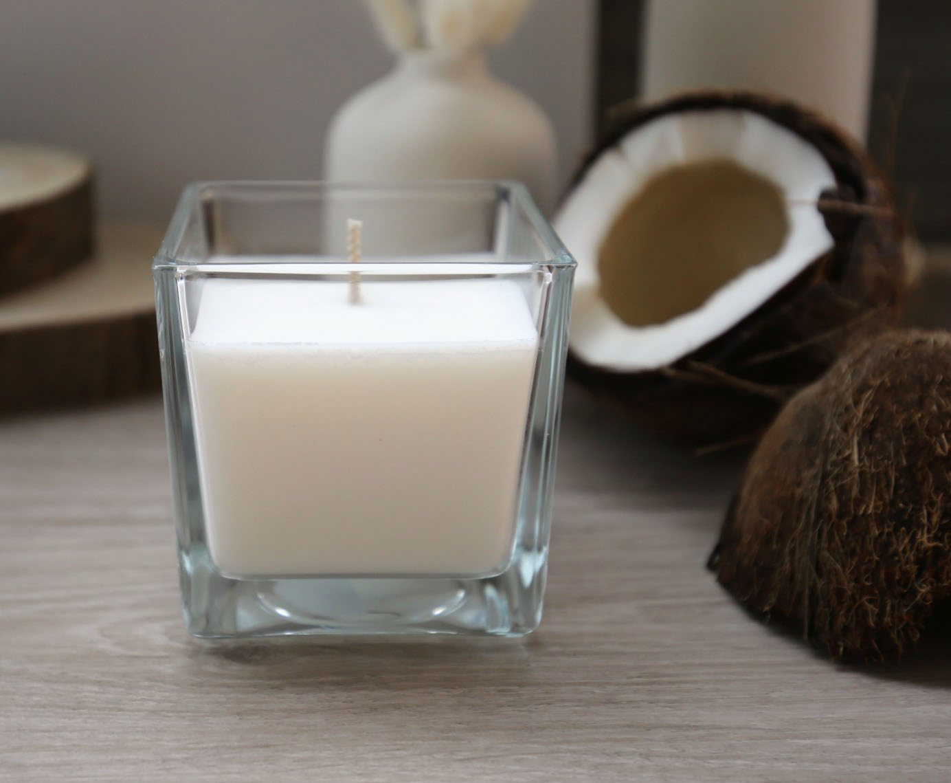 A square candle in a glass container surrounded by coconuts