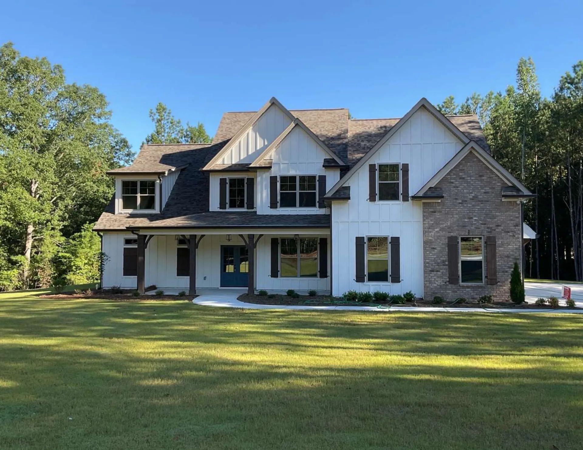 White farmhouse with gray and brick accents, blue door, and green lawn.