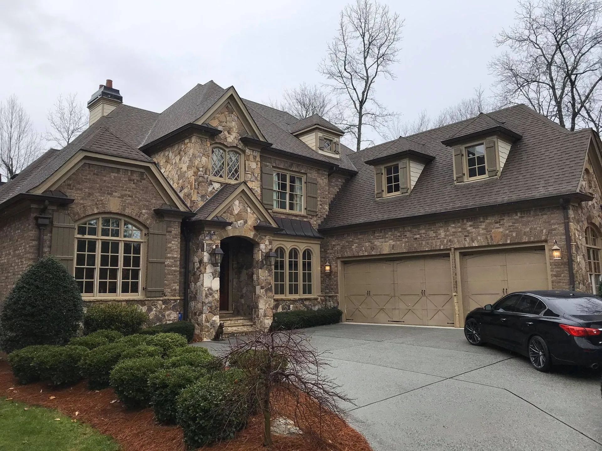 Large brick house with a brown roof and a two-car garage. A black car sits in the driveway.