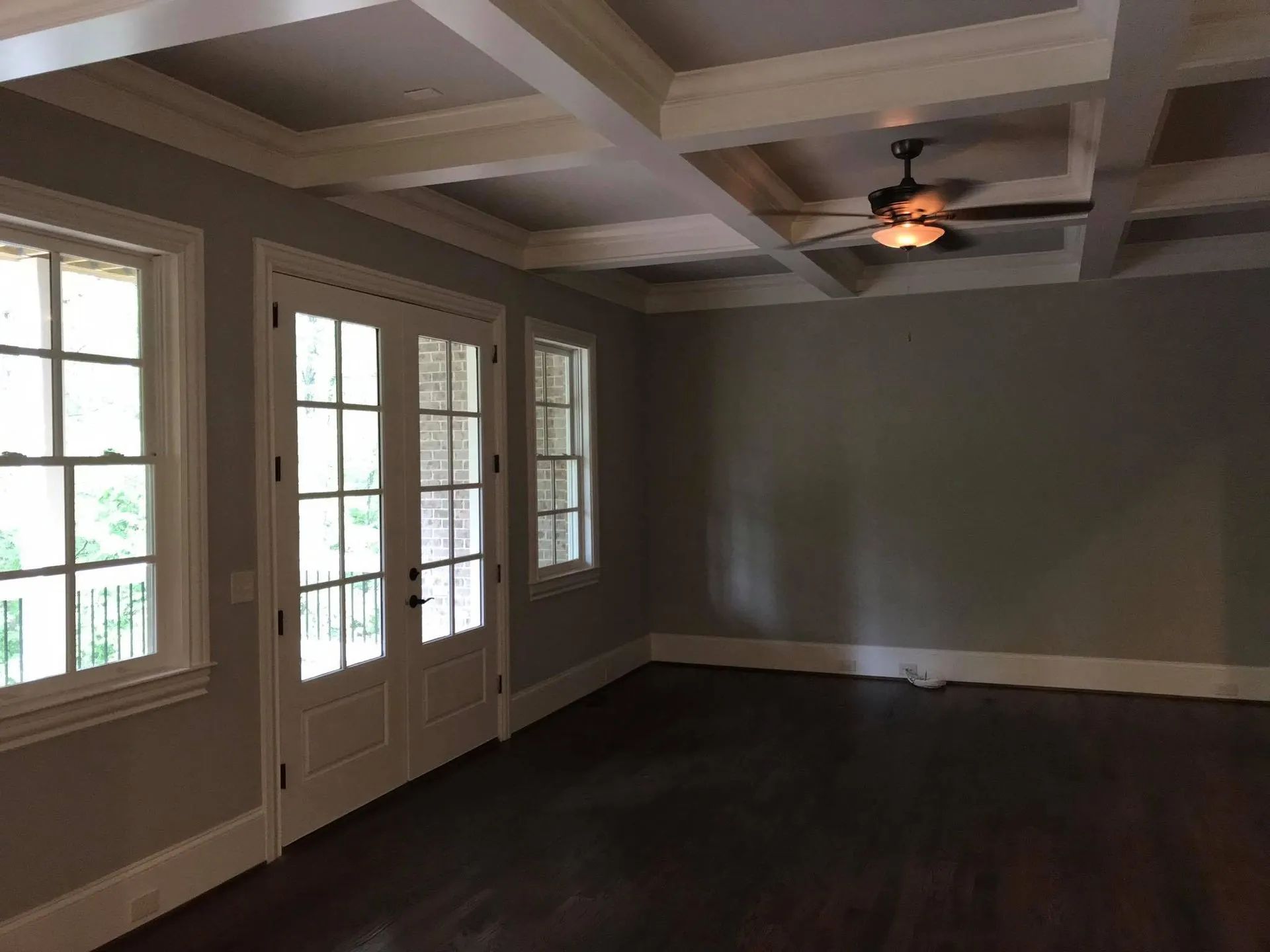 Empty room with gray walls, white trim, French doors, dark wood floor, and coffered ceiling.